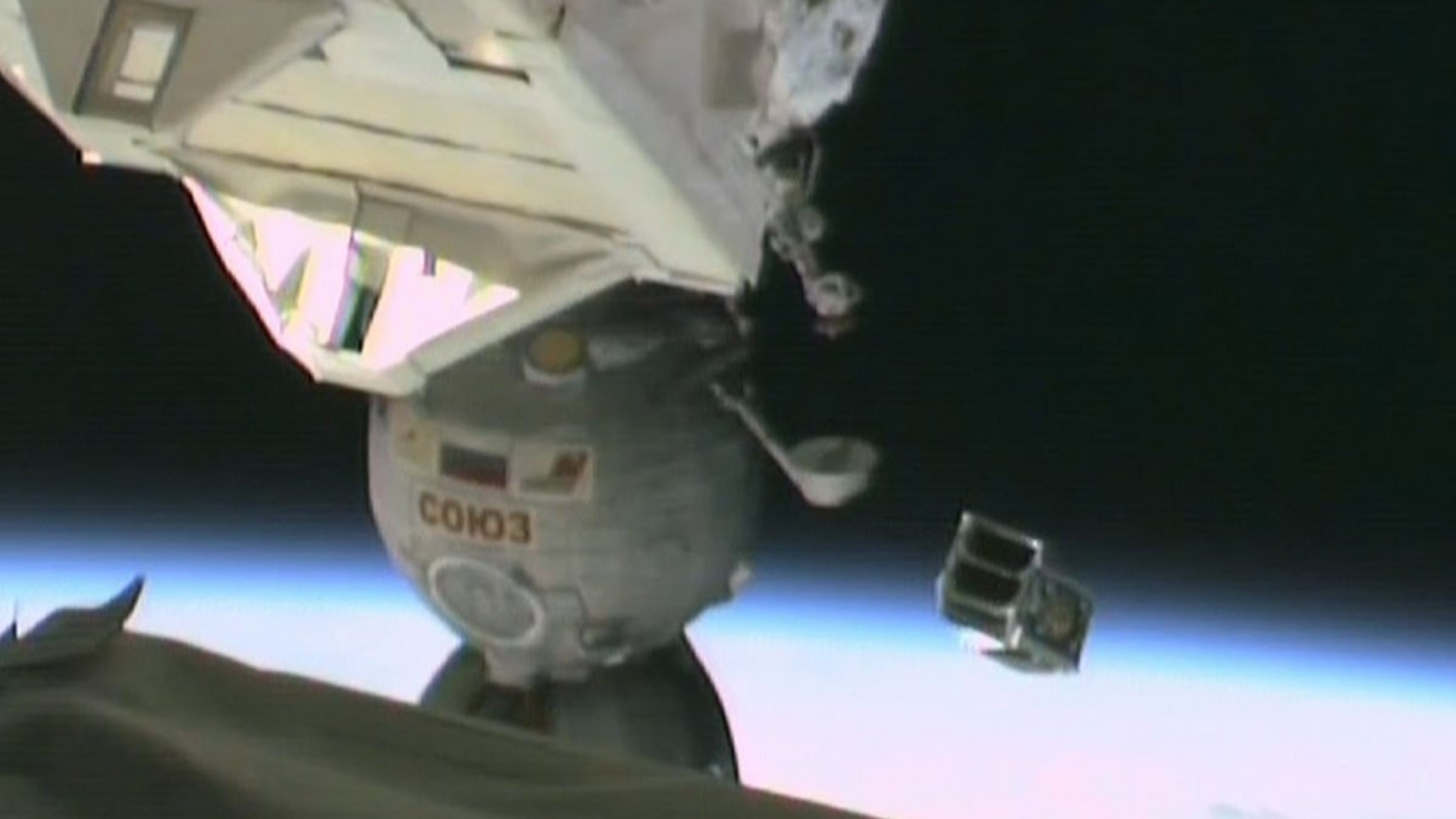 A small metal satellite is launched floating above Earth with part of the International Space Station seen on the left part of the image